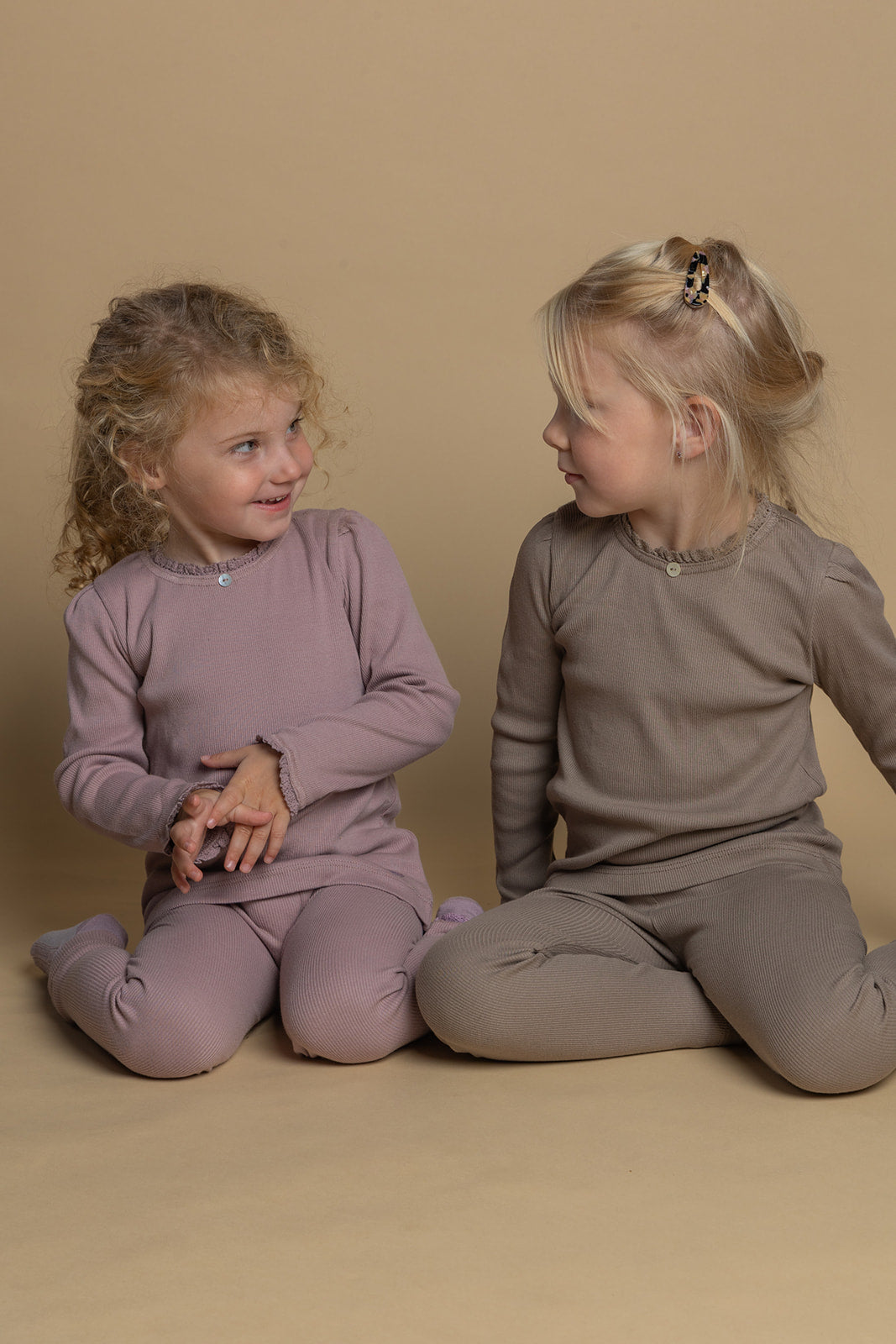 to piger sidder i matchende tøj-sæt i rosa og lys brun med leggings og bluse i økologisk bomuld med blondekanter